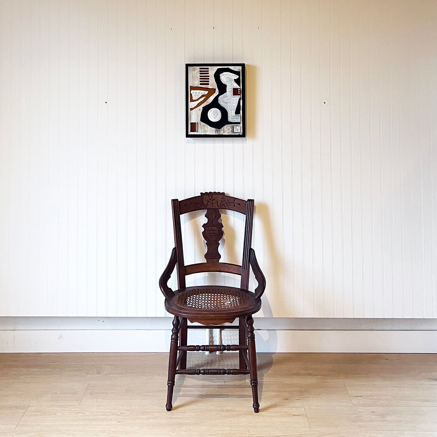 Small Leather and Acrylic art piece hanging on a white beadboard wall above a wood dining chair. Piece is entitled Just a Few Steps from the River by Angie Johnson.