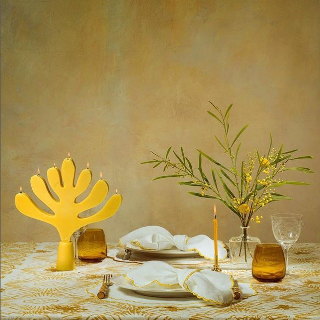 romantic table setting with candles, vases, napkins, glasses, plates in a yellow and cream hues. 