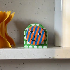 green and white polkadot, blue and orange striped face Metal Kitchen Timer placed on a shelf 