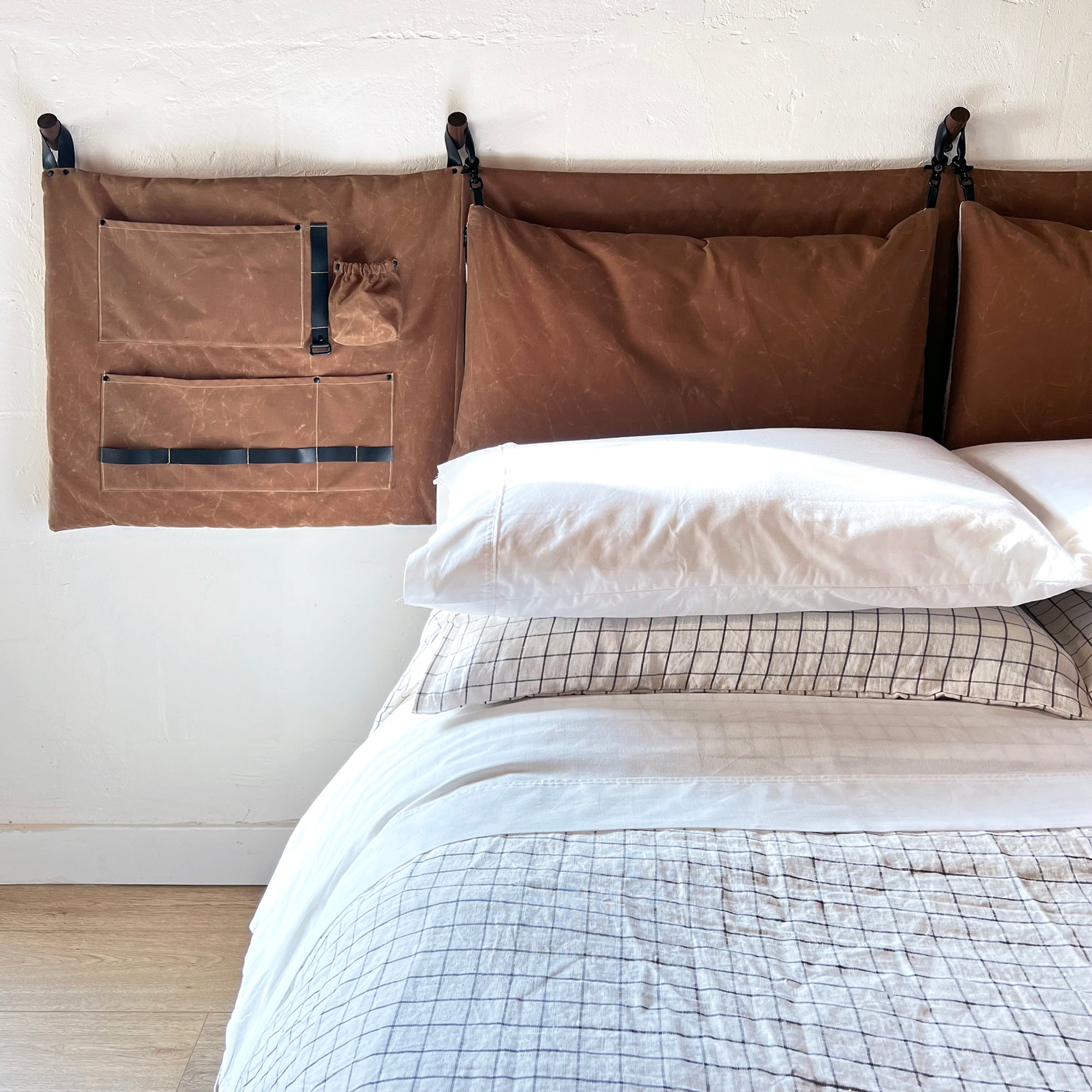 Half of the Camel Brown waxed cotton canvas scout headboard showcased above a made queen platform bed. 