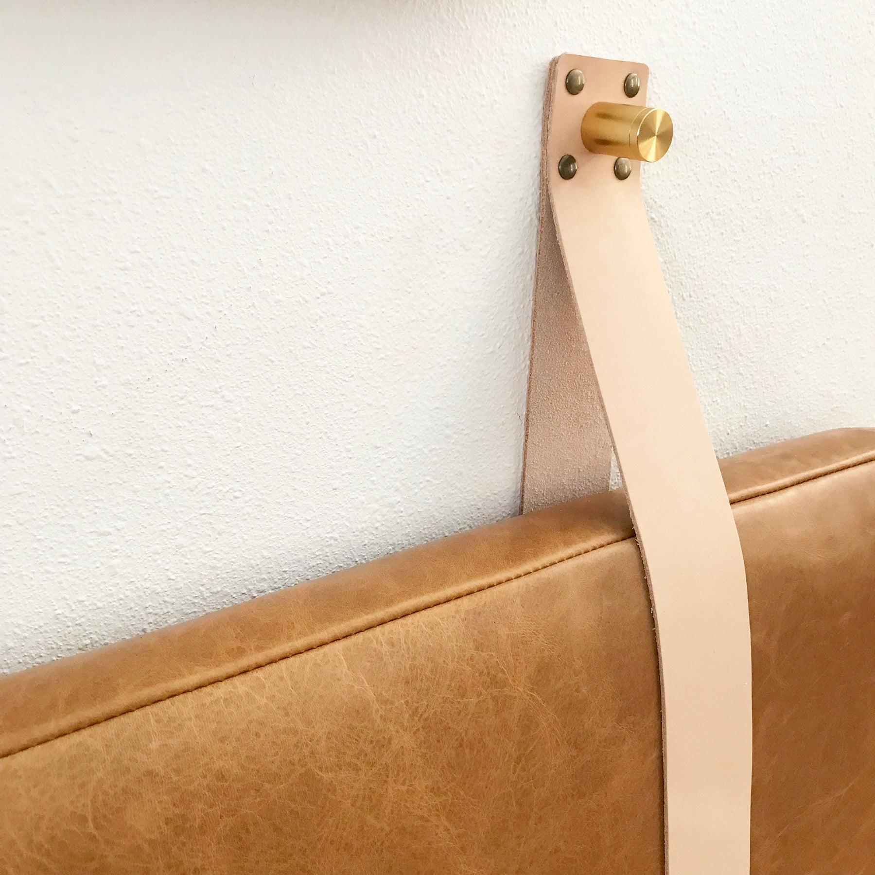 Close up of Natural Strap, Gold Standoff Hardware, Honey leather cushion headboard on a white wall