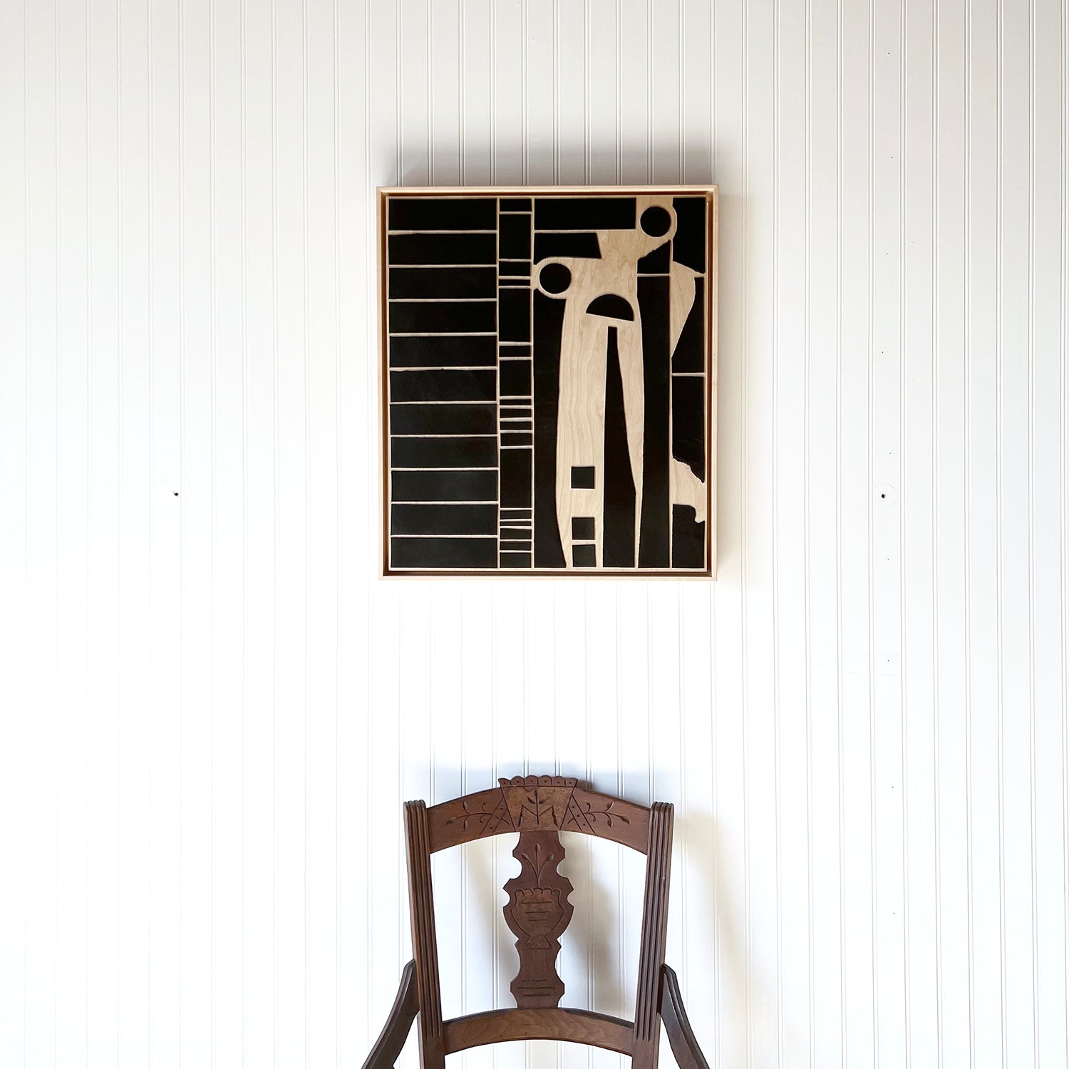 Abstract art made from Black leather on Wood by Los Angeles artist Angie Johnson hangs on a white wall above a wood chair