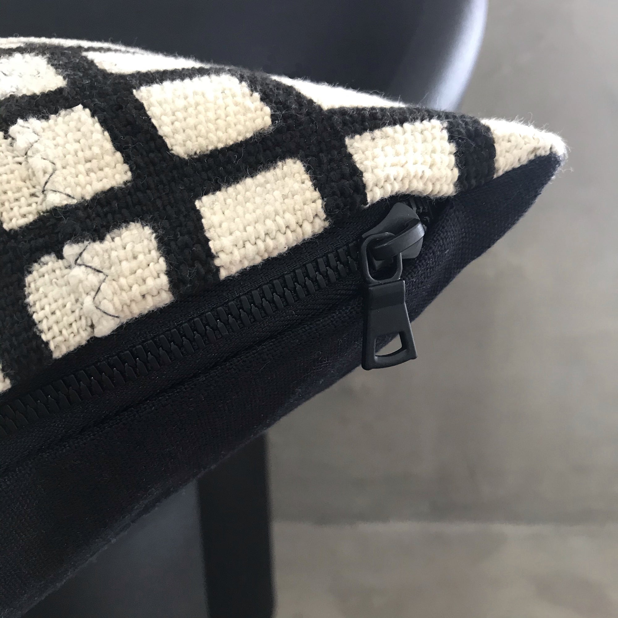 Detail of the black zip and zipper pull on the seam of the pillow.