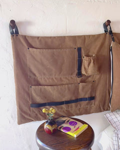 Video of the camel brown waxed cotton canvas scout headboard pockets being filled with magazines, books, eye glasses, ipad, iphone, water bottle, tech charging cords. 